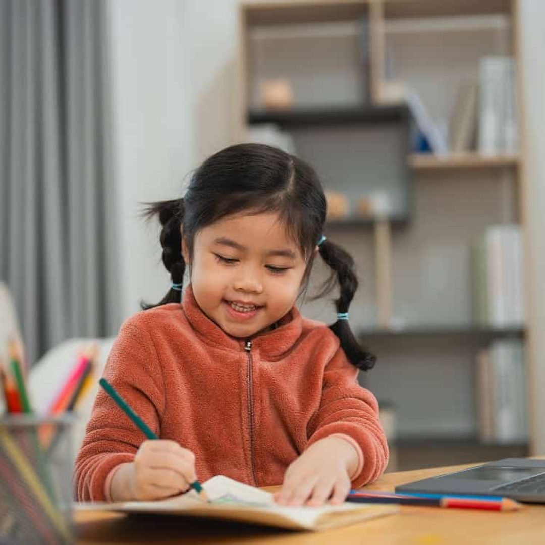 happy-child-drawing-with-color-pencils-home-cheerful-young-girl-with-pigtails-draws-contentedly-with-color-pencils-seated-her-home-desk-education-kids-concept